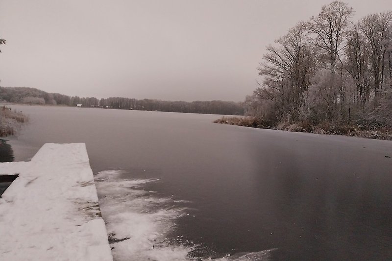 Blick auf ruhigen See mit winterlicher Landschaft - Winter 2023