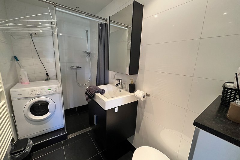 Badezimmer mit Waschmaschine, Spiegel und Waschbecken.