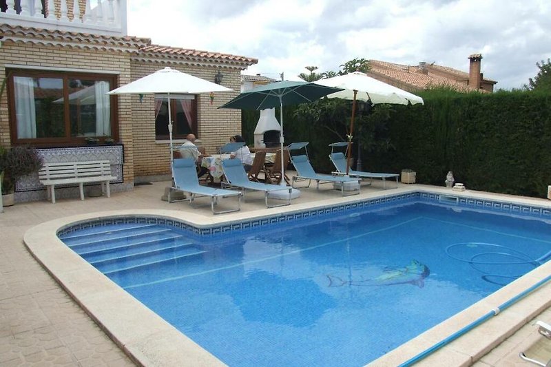 Schwimmbad mit Sonnenliegen und Sonnenschirmen in einer Ferienanlage.
