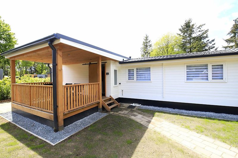 Een charmant huis met een houten veranda, omgeven door groen en een blauwe lucht.