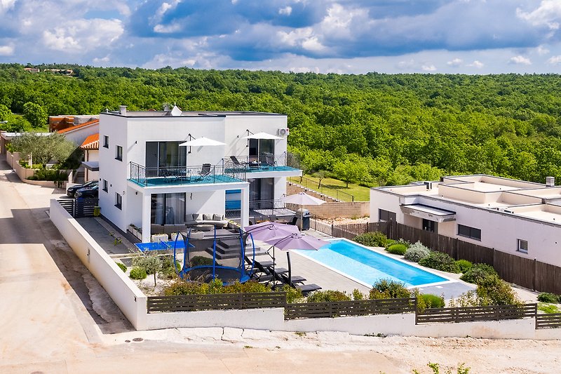 Elegante Villa mit Pool, umgeben von Natur und klarem Himmel.