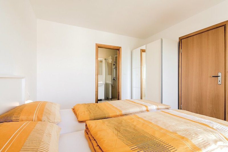 Udobna spavaća soba s drvenim krevetom i narančastim jastucima.