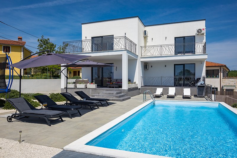 Luxuriöse Villa mit Pool, umgeben von Pflanzen und klarem Himmel.