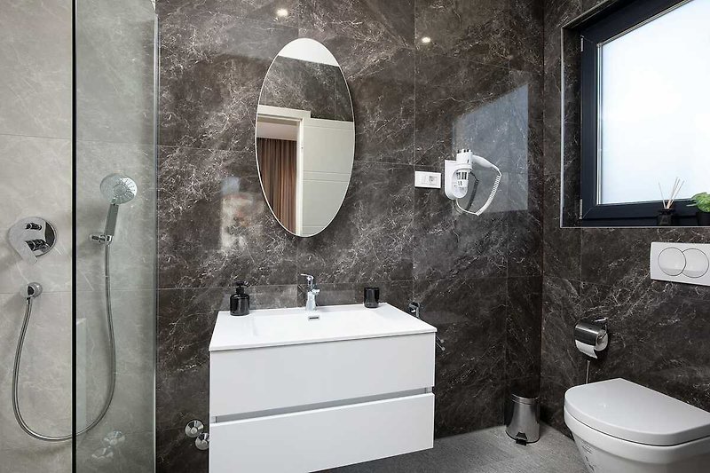 Moderan kupaonski prostor s bijelim umivaonikom, crnom slavinom i ogledalom.