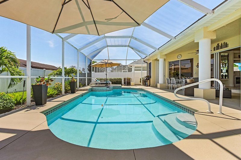 Schwimmbad mit Sonnenliegen und Palmen, umgeben von moderner Architektur.