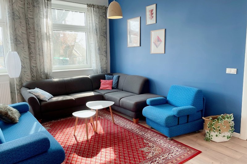 Gemütliches Wohnzimmer mit blauen Akzenten und Holzmöbeln. Entspannen Sie auf dem Sofa und genießen Sie den Ausblick aus dem Fenster.