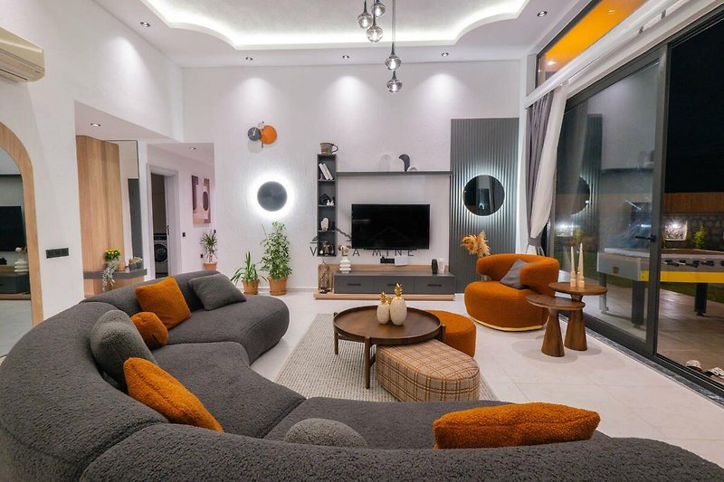 Wohnzimmer mit bequemer Couch, Holzmöbeln, Tisch, Fernseher und Beleuchtung.
