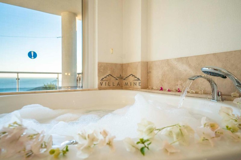 Luxuriöses Badezimmer mit Jacuzzi, Blumen und Glasdetails.
