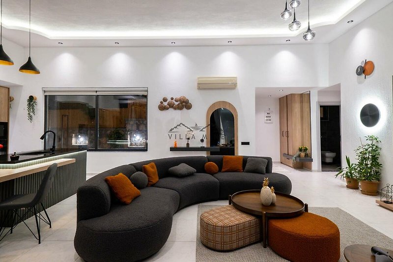 Wohnzimmer mit bequemer Couch, Möbeln, Tisch, Pflanze und Beleuchtung.