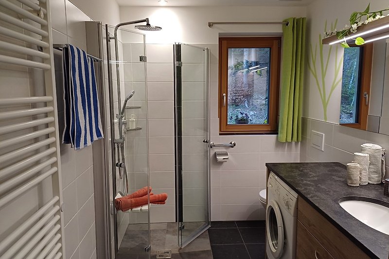 Badezimmer mit Waschtisch, Dusche, Waschmaschine und Fenster.