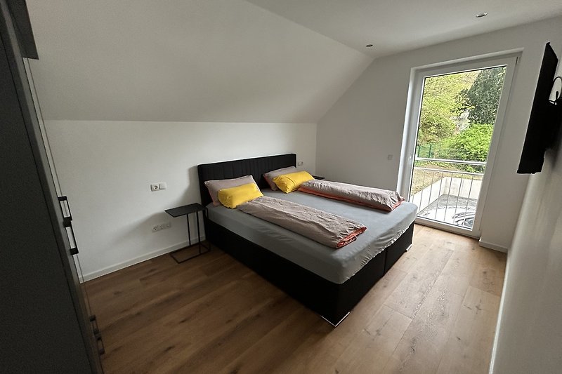 Schlafzimmer mit bequemem Bett, Fenster und Holzdecke.