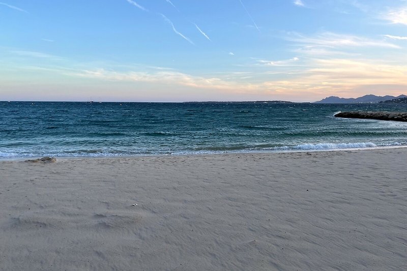 Genießen Sie die ruhige Dämmerung am Strand mit azurblauem Wasser und sanften Wellen.