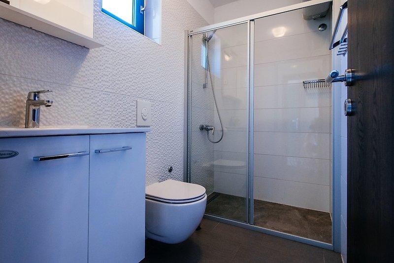 Plavi umivaonik, tuš, ogledalo i kupaonski ormar u ljubičastoj kupaonici.