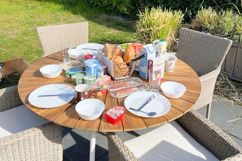 Sommerliches Picknick im Garten mit Tisch, Stühlen und Essen.