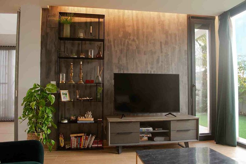 Wohnzimmer mit Fernseher, Couch, Holzmöbeln und Pflanzen.