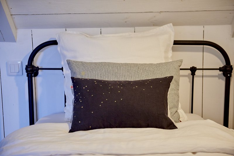 Chambre confortable avec lit en bois, oreillers moelleux et lampe grise.