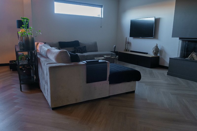 Gemütliches Wohnzimmer mit Holzboden, bequemer Couch und Fernseher.
