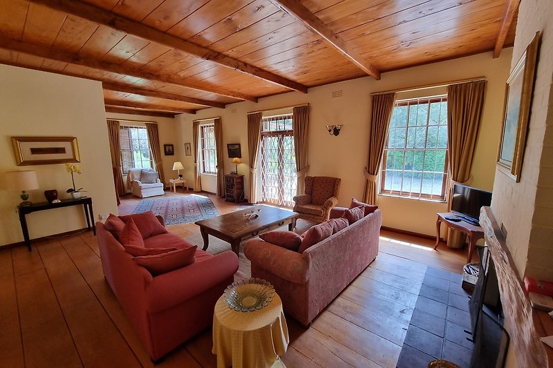 Gemütliches Wohnzimmer mit Holzbalken und boden, gemütliche Couches und große Fenster.