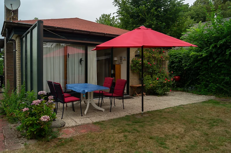 Garten mit Terrasse, Möbeln und Sonnenschirm.