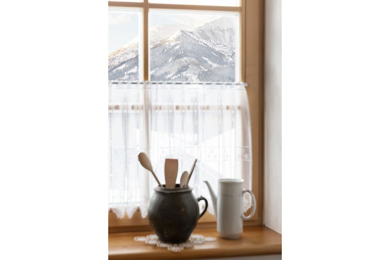 Fensterblick auf verschneite Berge, Tee und Kaffee in Porzellangeschirr.
