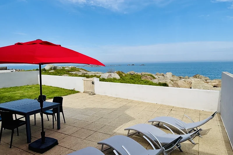 Direkter Meerblick mit Sonnenliegen, Schirm und Outdoor-Tisch am Strand.