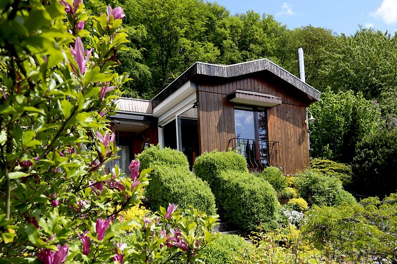 Schönes Ferienhaus mit blühenden Pflanzen, grünem Garten und malerischer Landschaft.