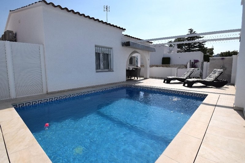 Schwimmbad mit Sonnenliegen, umgeben von einer schönen Landschaft und einem gemütlichen Haus.