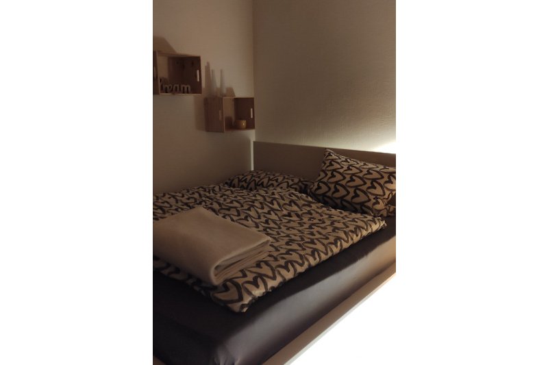 Das Doppelbett im Wohnzimmer wird stilvoll beleuchtet und bietet praktische Ablagefächer
