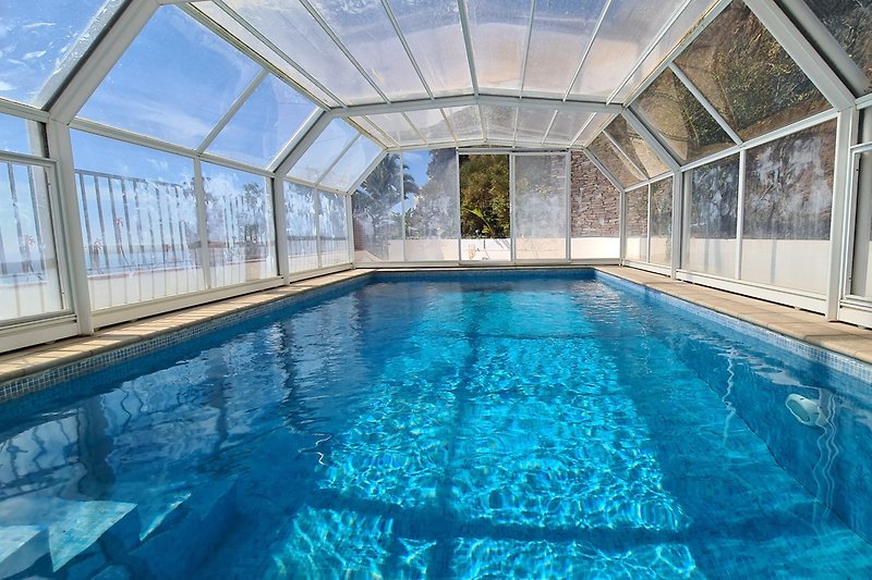 Ganzjähriger Pool im Winter mit Verglasung zugezogen, umgeben von Pflanzen und Felsen - mit Blick aufs Mittelmeer.