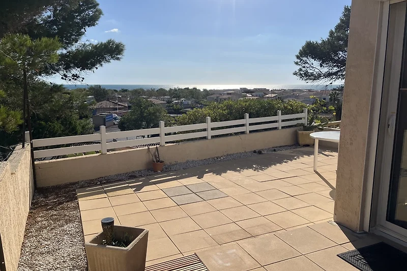 Sonnige Terrasse mit Balkon, Möbeln und schattigem Gehweg.