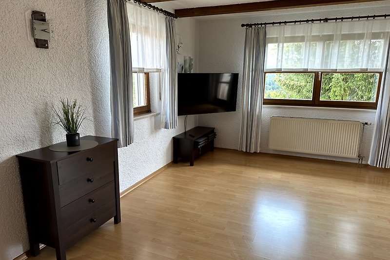 Gemütliches Wohnzimmer mit Holzmöbeln und großen Fenstern.