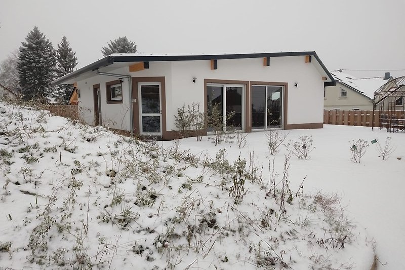 Ein winterliches Haus mit Schnee, einem Holzdach und einem Fenster.