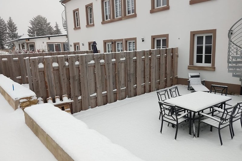 Schneebedecktes Ferienhaus mit Holzveranda und Winterlandschaft.