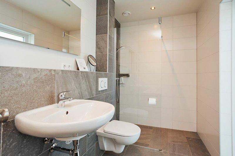 Een moderne badkamer met spiegel, kraan, wastafel en douche.