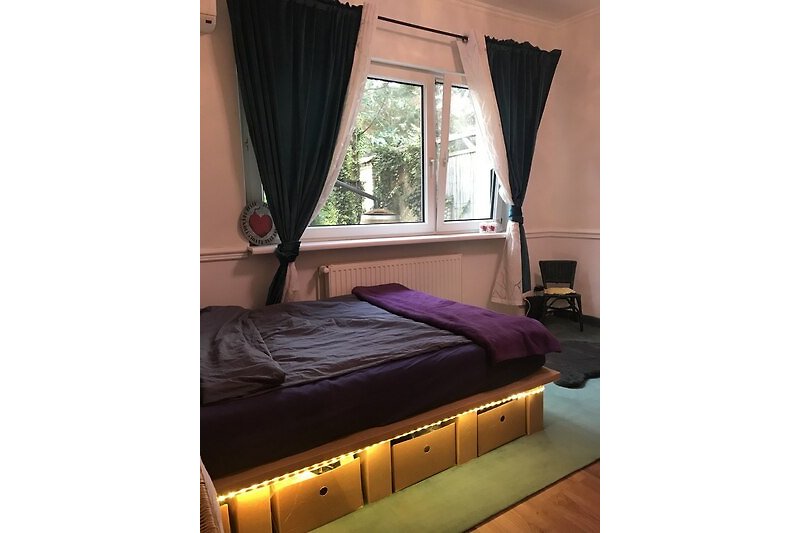 Gemütliches Schlafzimmer mit lila Vorhängen und bequemem Bett.