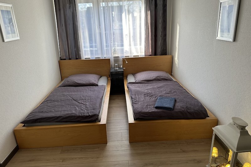 Gemütliches Schlafzimmer mit Holzbett, Vorhängen und gemütlicher Bettwäsche.