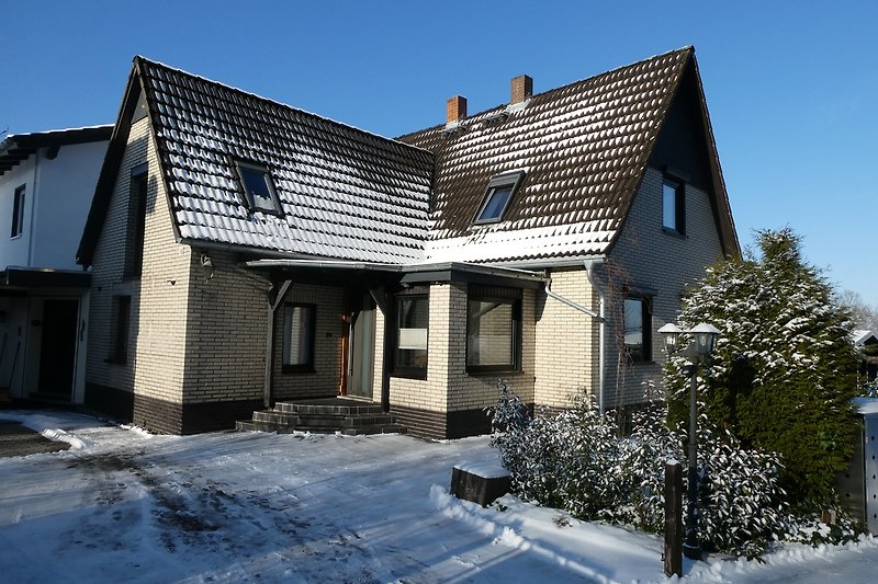 Schönes Winterhaus mit verschneitem Dach und gemütlicher Veranda.