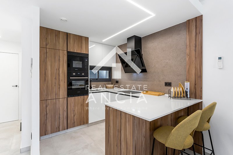 Moderne Küche mit Holzoberflächen, stilvoller Beleuchtung und Küchengeräten.