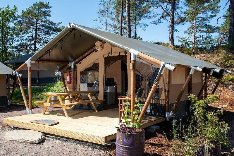 Holzunterstand mit Zelt, Stühlen und Tisch im Freien.