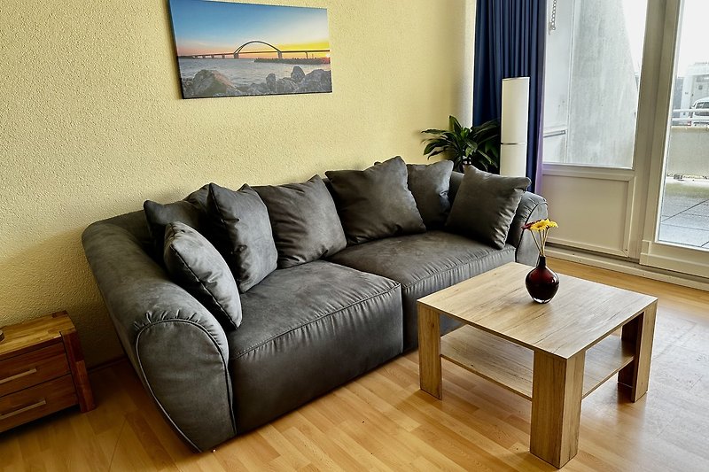 Gemütliches Wohnzimmer mit bequemer Couch, Holzmöbeln und großen Fenstern.