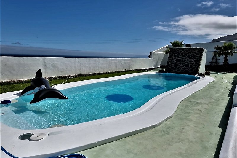 Schönes Haus mit Pool, umgeben von tropischer Landschaft und blauem Himmel.