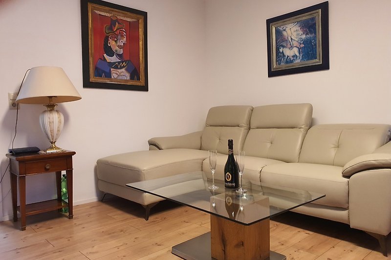 Wohnzimmer mit bequemer Couch, Tisch, Lampen & Bilderrahmen.