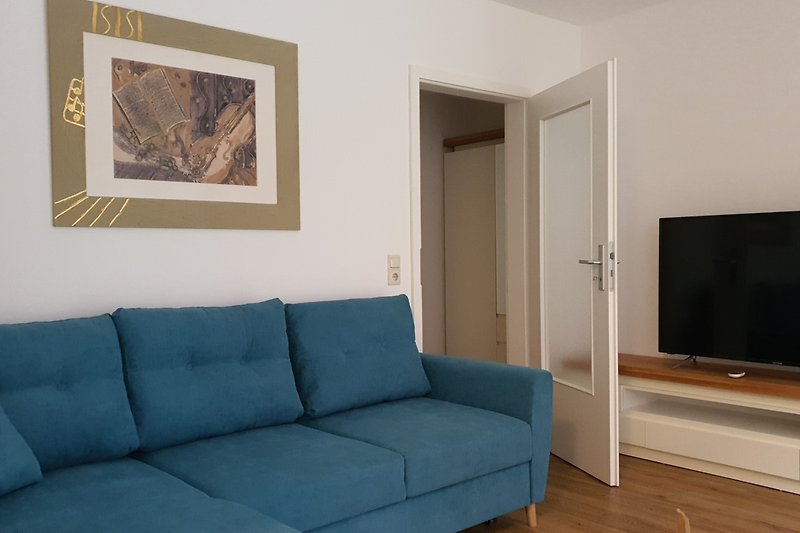 Wohnzimmer mit gemütlicher Eckcouch, Couchtisch, TV-Board, Smartfernseher und Zugang zur Diele mit Garderobenschrank
