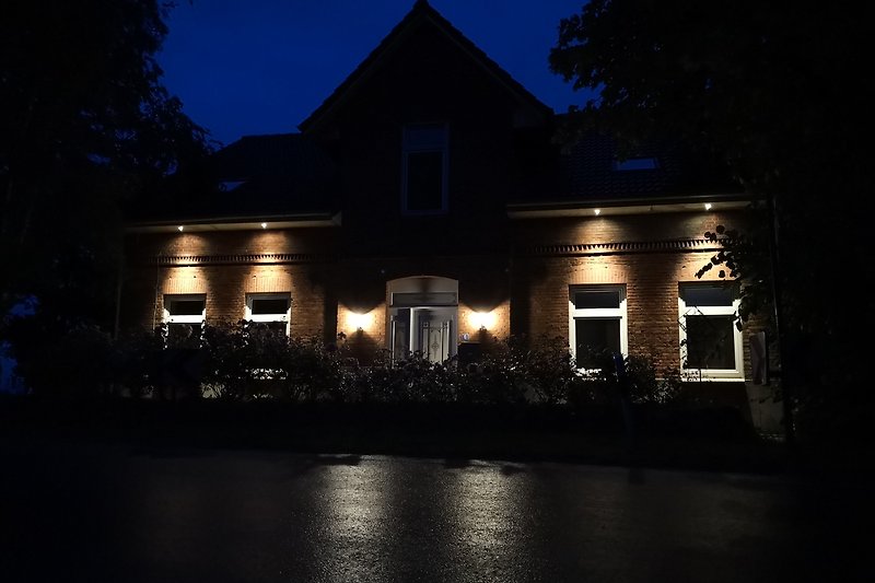 Charmantes Haus bei Nacht mit beleuchteter Fassade und Garten.