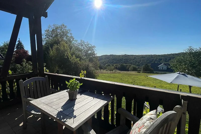 Überdachte Veranda mit Sitzgruppe, Holztisch und Blick ins Grüne.