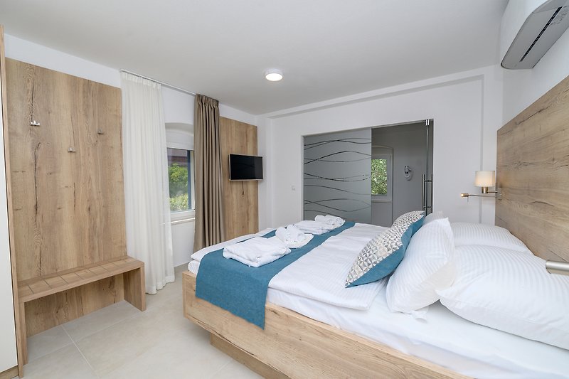 Gemütliches Schlafzimmer mit Holzbett, bequemer Matratze und stilvollem Bettzeug und Fernseher.