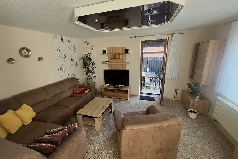 Großzügiges Wohnzimmer mit Sofa, Sessel, TV und Zugang zur Terrasse.