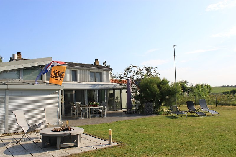 Haus mit Terrasse, Garten, Bäumen und Pflanzen.