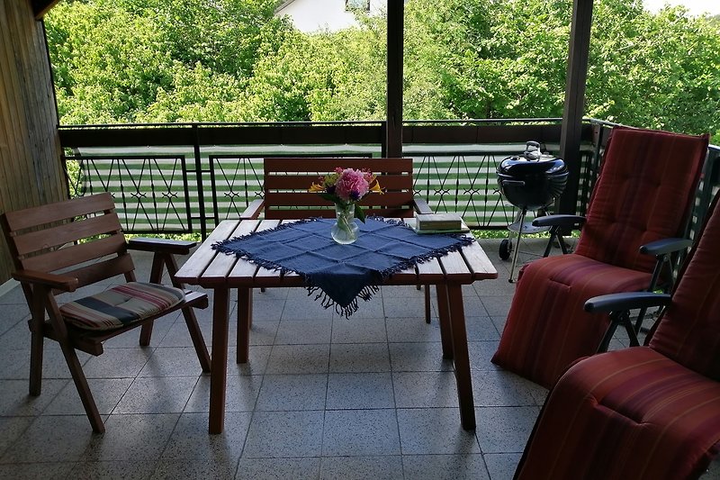 Große, überdachte Terrasse mit Tisch, Stühlen und Blumen und Grillmöglichkeit