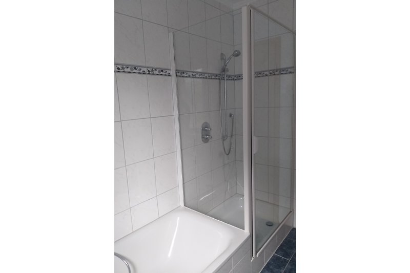 Ein modernes Badezimmer mit weißen Fliesen und Glasdusche.